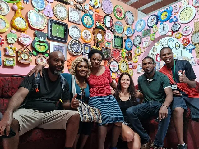 Group of people posing in a room covered with numerous clocks on the wall.